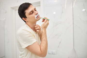 Man grooming face with shaving cream and razor during morning routine