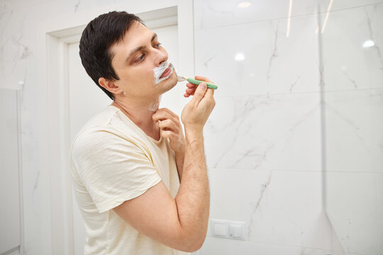 Man grooming face with shaving cream and razor during morning routine
