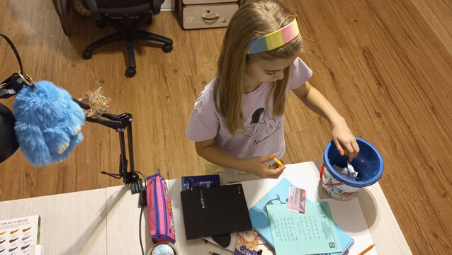 Young girl organizing craft supplies at home workspace with blue bucket  