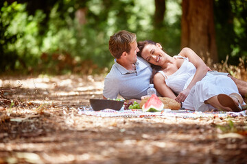 Happy, couple and relax with picnic in forest for anniversary celebration, weekend break or bonding. Love, people and romantic date with snacks for outdoor brunch, relationship support and trust
