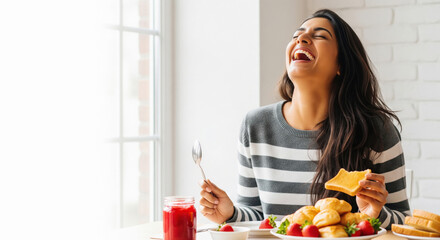 A joyful young Indian woman in a striped sweater laughs heartily while enjoying a bright breakfast of toast, pastries, and strawberries