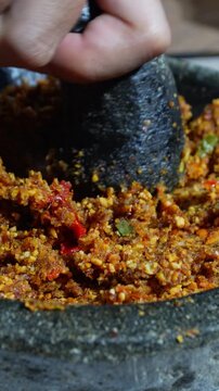Homemade peanut chili sauce being ground in a stone mortar. Traditional Indonesian sambal making process. 4k vertical concept
