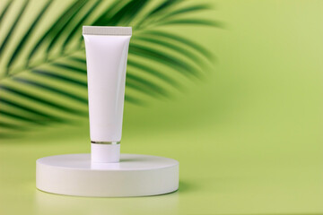 empty white cream tube on a white round shaped podium against light green background with soft shadow of leaves and copy space