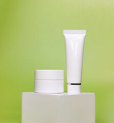 empty white jar and tube of cosmetic cream on a white square shaped podium against light green background. cosmetic mockup display