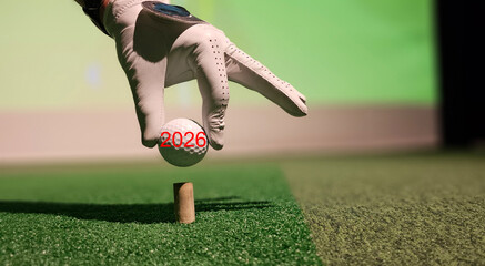 Hand placing a golf ball on a tee during a practice session at an indoor facility in 2026 concept