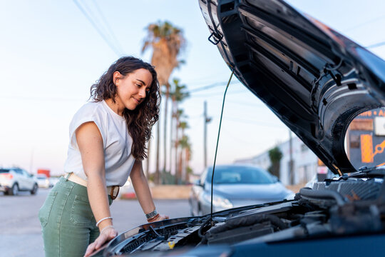 Woman inspecting car engine by roadside after breakdown - Powered by Adobe