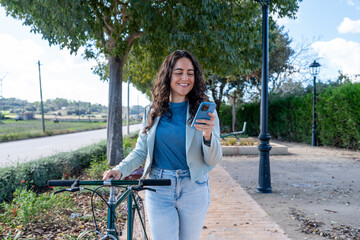 Woman walking bicycle checking smartphone on urban commute