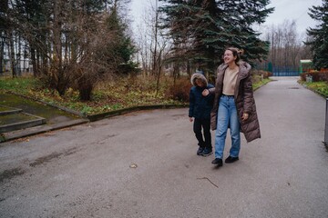 Fototapeta premium A young mother picks up her son from school, walking home together with joyful smiles. Authentic moment of family love, education, and daily parenting routine