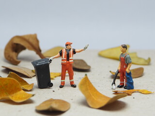 Mini toy of action figure at outdoor with blurred background. Miniature photography concept design. Minifigure of cleaning crew with dried leaves and garbage truck.
