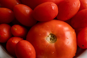 bunch of tomatoes and cherry tomatoes in a white bowl on dark background