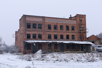 Old derelict brick building stands in winter scenery with signs of long-term neglect. Concept of disappearing industry, architectural history, educational materials and urban studies.