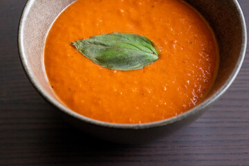 creamy roasted tomato and red pepper soup in black bowl with fresh basil