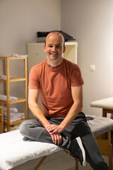 Fototapeta premium Man smiling while receiving a leg stretch from a physical therapist on a table in a clinic, focusing on rehabilitation and health