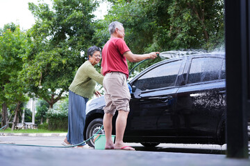 Senior Couple Washing A Car Together Outdoors, Elderly Man And Woman Cleaning Their Vehicle With A Hose, Happy Senior Couple Doing A Car Wash At Home Driveway
