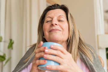 Mature woman enjoying a peaceful moment, relaxing eyes closed and warming herself with a mug