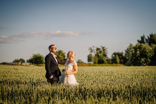 Couple in formal attire standing in a lush green field during sunset, embracing each other with joy, capturing a romantic moment in nature's beauty - Powered by Adobe