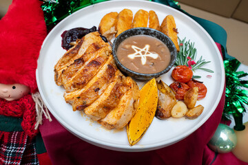A Christmas-themed food arrangement on a plate, including chicken and vegetables, with a Christmas doll decoration on the side