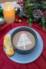 Christmas soup artfully decorated, accompanied by bread. The table is adorned with festive decorations, including a lit candle and ornaments