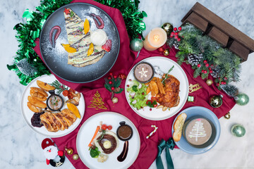 A festive Christmas food spread with a variety of dishes and decorations. The culinary creations are arranged on a red tablecloth, accompanied by decorative elements and a festive atmosphere. 