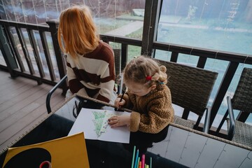 A 4-year-old girl and her older sister draw greeting cards for their parents together. Authentic...