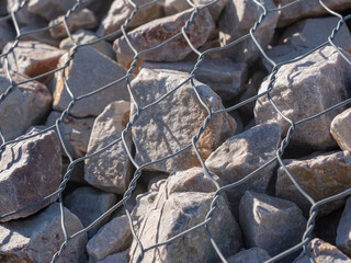 Gabion stone wall construction close up. New stone fence in wire grid, iron cage with rocks