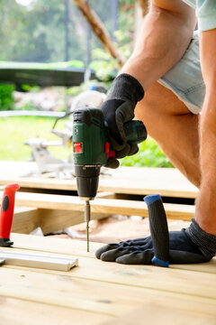 Homeowner using a power drill to install wooden deck planks during a backyard renovation, capturing realistic DIY, woodworking, outdoor construction.