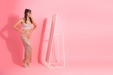Glamour fashion scene with a young woman in a pink sequin dress standing beside standing mirror against a pink backdrop chic stylish beauty and confidence