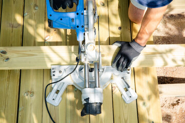 Professional carpenter cutting deck planks with a miter saw during outdoor construction, showing skilled craftsmanship, precise home renovation work.