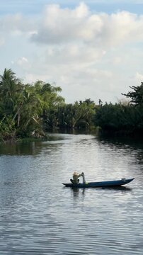 Fisherman in small boat casting net on tropical river with palm-lined shore