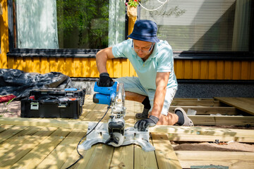 Fototapeta premium Professional carpenter cutting deck planks with a miter saw during outdoor construction, showing skilled craftsmanship, precise home renovation work.