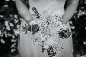 Bride holding a beautiful bouquet of white and green flowers, surrounded by lush greenery,...