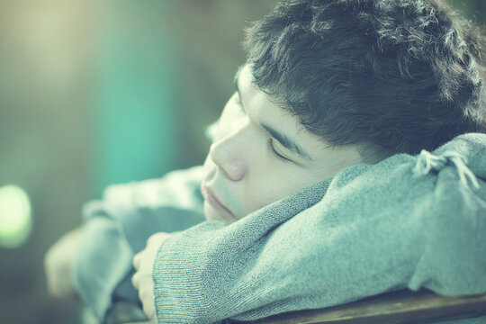 Young man resting on folded arms in soft light with calm expression