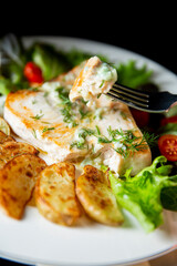 Delicious fried swordfish steak with roasted potato wedges, fresh greens, and creamy sauce. Healthy seafood dinner meal concept.