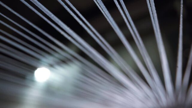 Tight parallel textile threads stretch toward a bright light source, forming converging lines that reveal tension, symmetry and motion inside an active industrial weaving loom
