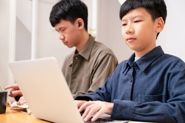 Two smart looking Asian boy study online learning, type on computer laptop and digital tablet, with concentration and focus at home in white house. Modern homeschool education, e-learning technology