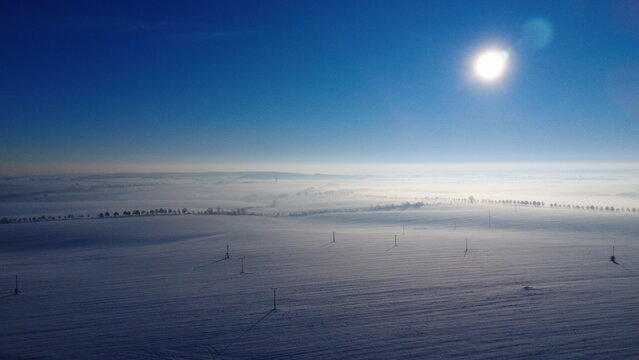 sunny day, snowy field, winter landscape, Czech countryside, aerial drone view, bright sky, fresh snow, open farmland, peaceful atmosphere, winter scenery - Powered by Adobe