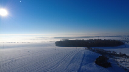 sunny day, snowy field, winter landscape, Czech countryside, aerial drone view, bright sky, fresh snow, open farmland, peaceful atmosphere, winter scenery