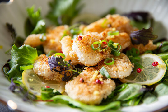 Crispy panko cod cheeks served on fresh gourmet greens with lemon and pink peppercorns - a premium seafood dish for fine dining menus and culinary