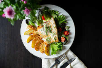 Delicious fried swordfish steak with roasted potato wedges, fresh greens, and creamy sauce. Healthy seafood dinner meal concept.