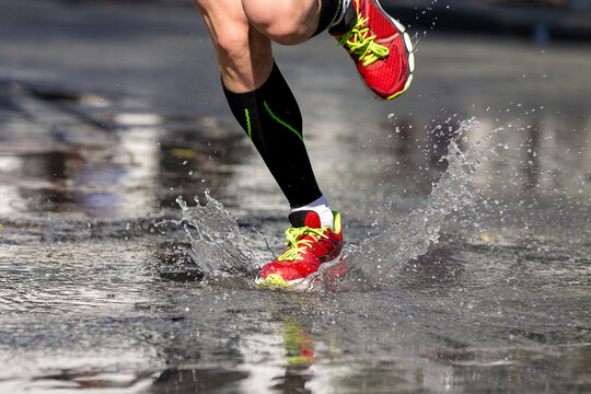 Runner feet in compression socks running in splashes of water on asphalt - Powered by Adobe