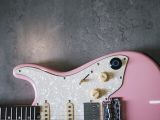 Pink electric guitar on a textured gray background, top view. A close-up shot of a pink electric guitar shows the details of the instrument against a neutral backdrop