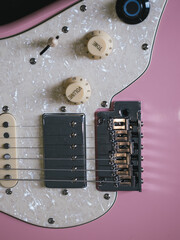 Close-up of a pink electric guitar with pearl pickguard and chrome hardware. This image showcases the details of an electric guitar, highlighting its components and design elements