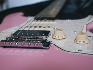 Close-up of a pink electric guitar with white pearloid pickguard and knobs. This image showcases the details of an electric guitar, highlighting its design and components