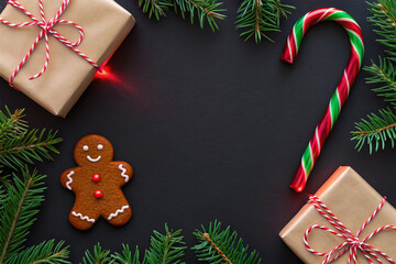 Festive Christmas flat lay with beautifully wrapped gift boxes, fir tree branches, a gingerbread man cookie, and a candy cane on a dark background, perfect for holiday greetings and seasonal design