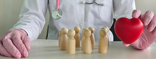 Doctor in lab coat holding red heart with wooden figures symbolizing patients in a medical...