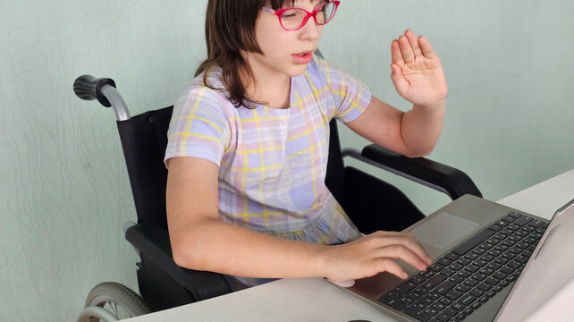 Girl in wheelchair happily using laptop while giving thumbs up during online learning session concept