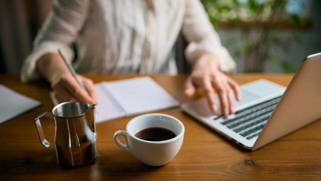 Coffee and metal pitcher on office desk during active work. Concept of office lifestyle, beverage presentation, productivity routines, and morning preparation materials.