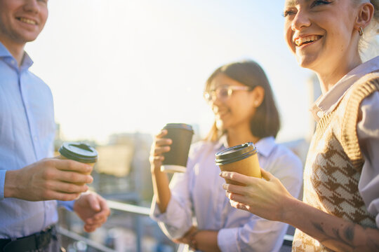 Coworkers holding takeaway coffee cups while talking outdoors. Concept of energizing breaks, informal team chats, workplace wellbeing, and short social pauses during the day.