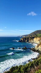 Fototapeta premium Coastal vista of ocean meeting cliffs under a bright blue sky