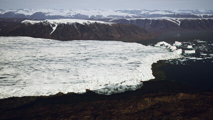 Towering mountains surround a vast expanse of ice where large chunks break off a glacier and crash into the blue ocean. The scene captures the beauty and power of nature in a remote region.